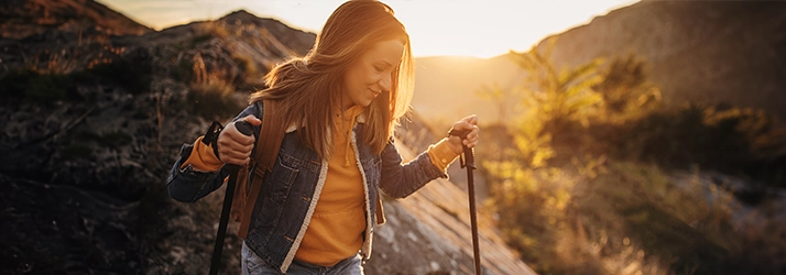 Person hiking in a mountain landscape at sunset, representing an active lifestyle, outdoor wellness, and physical endurance.
